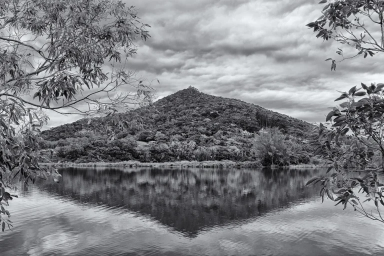 Lagoa de Ibiraquera em preto e branco, com espelho d'água calmo, vegetação na margem e morro ao fundo