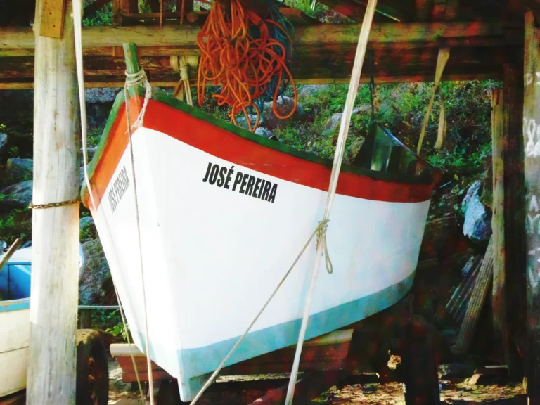 Barco de pesca branco com faixa vermelha guardado num rancho de madeira na Praia da Vila
