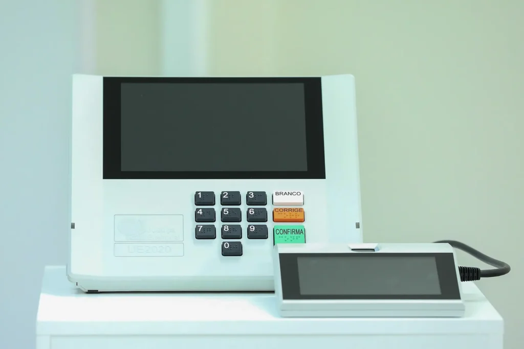 Urna eletrônica brasileira modelo UE2020 com o terminal do mesário ao lado, sobre uma mesa branca