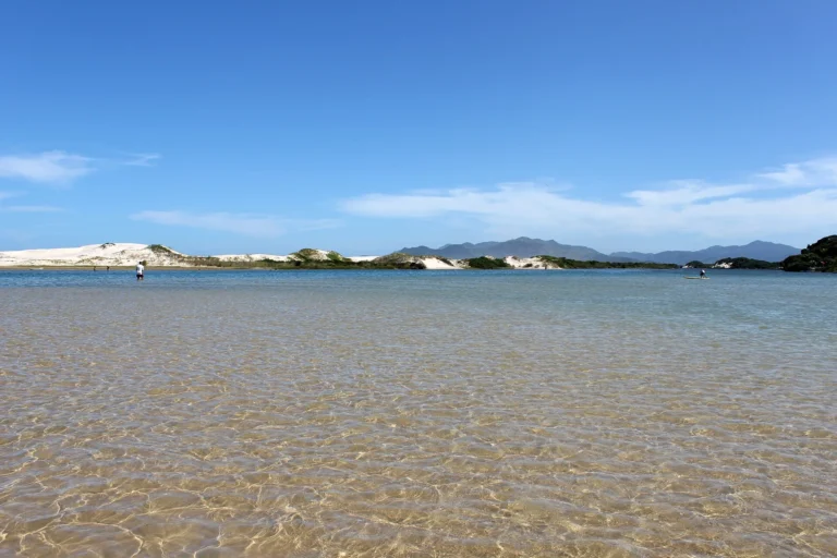 Águas rasas e transparentes do Rio da Madre na travessia para a Praia da Guarda do Embaú, com dunas e morros ao fundo