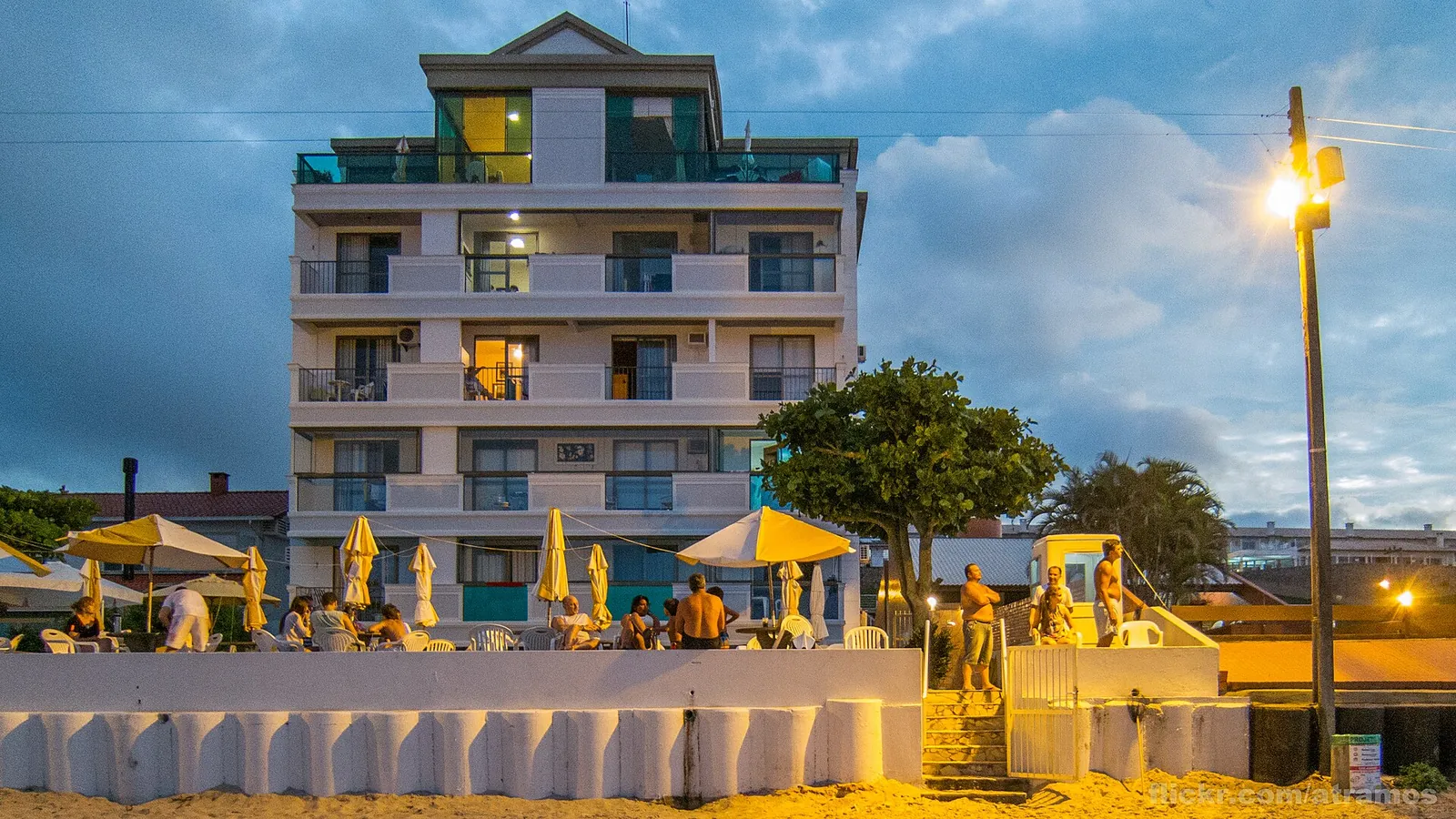 Hotel de vários andares iluminado ao entardecer, de frente para a praia em Florianópolis, com guarda-sóis à frente