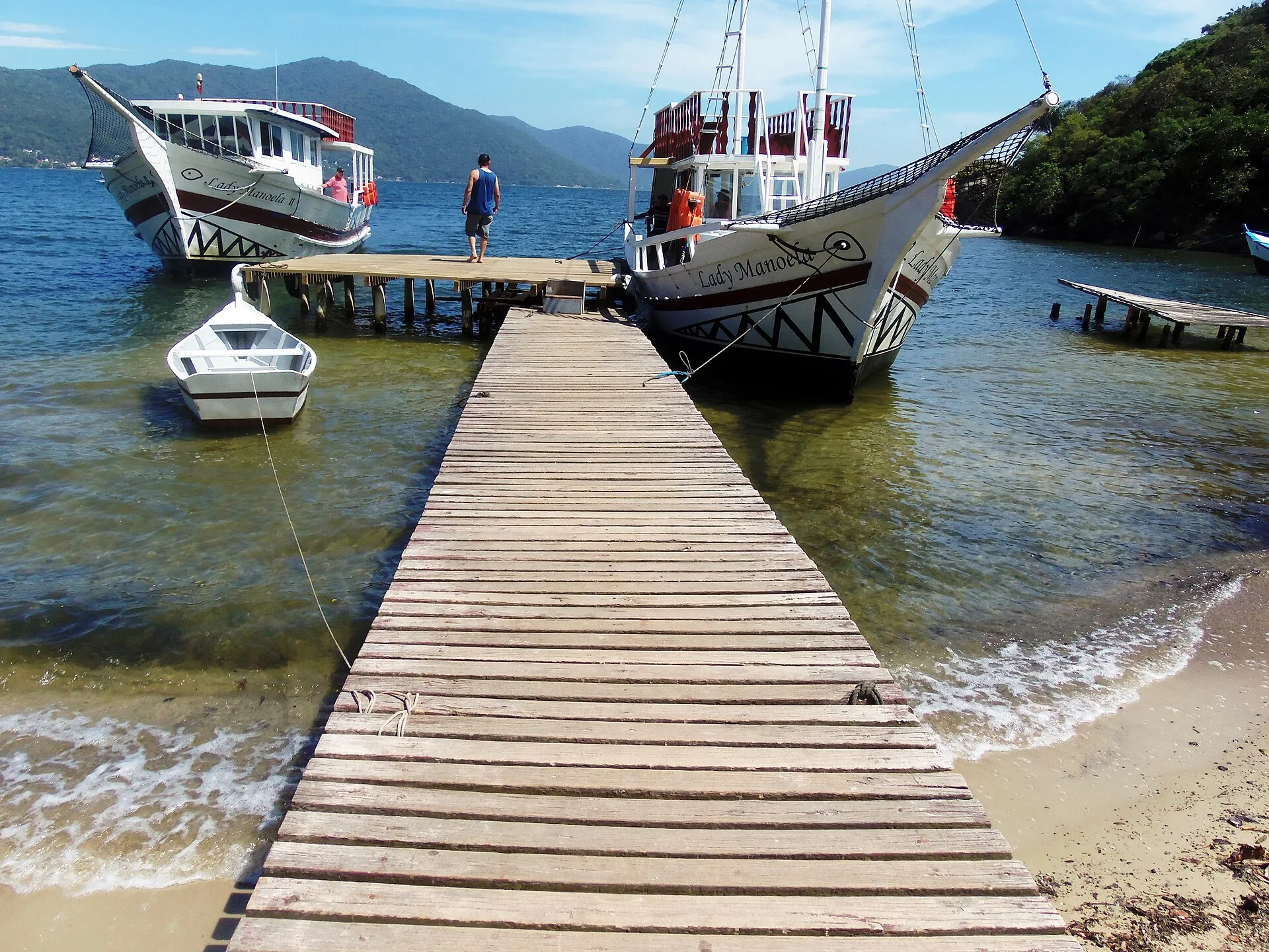 Trapiche de madeira sobre a água da Lagoa da Conceição, com barcos de passeio atracados e morros ao fundo