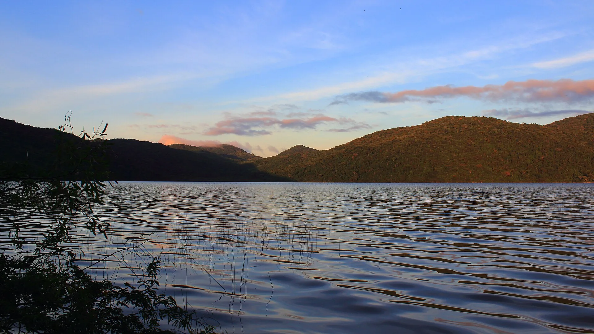 Amanhecer na Lagoa do Peri, com céu alaranjado sobre os morros e a água escura em primeiro plano