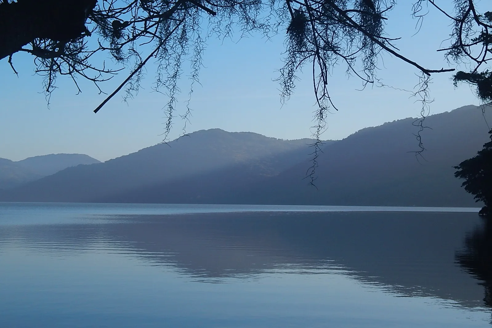 Lagoa do Peri vista do canto norte, com a água calma refletindo morros de mata e céu claro