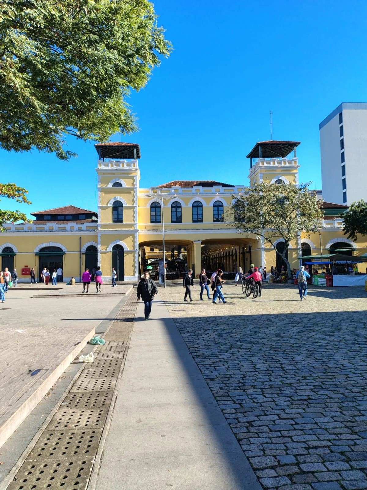 Mercado Público de Florianópolis visto do Largo da Alfândega, com o calçadão de pedra em primeiro plano e pessoas caminhando