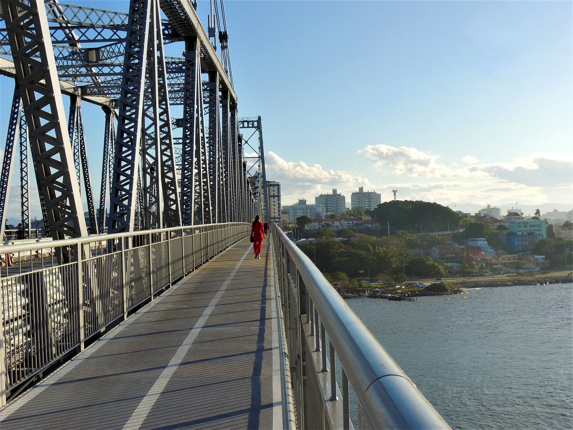 Passarela de pedestres da Ponte Hercílio Luz com treliças metálicas e grade de proteção, com a baía ao fundo