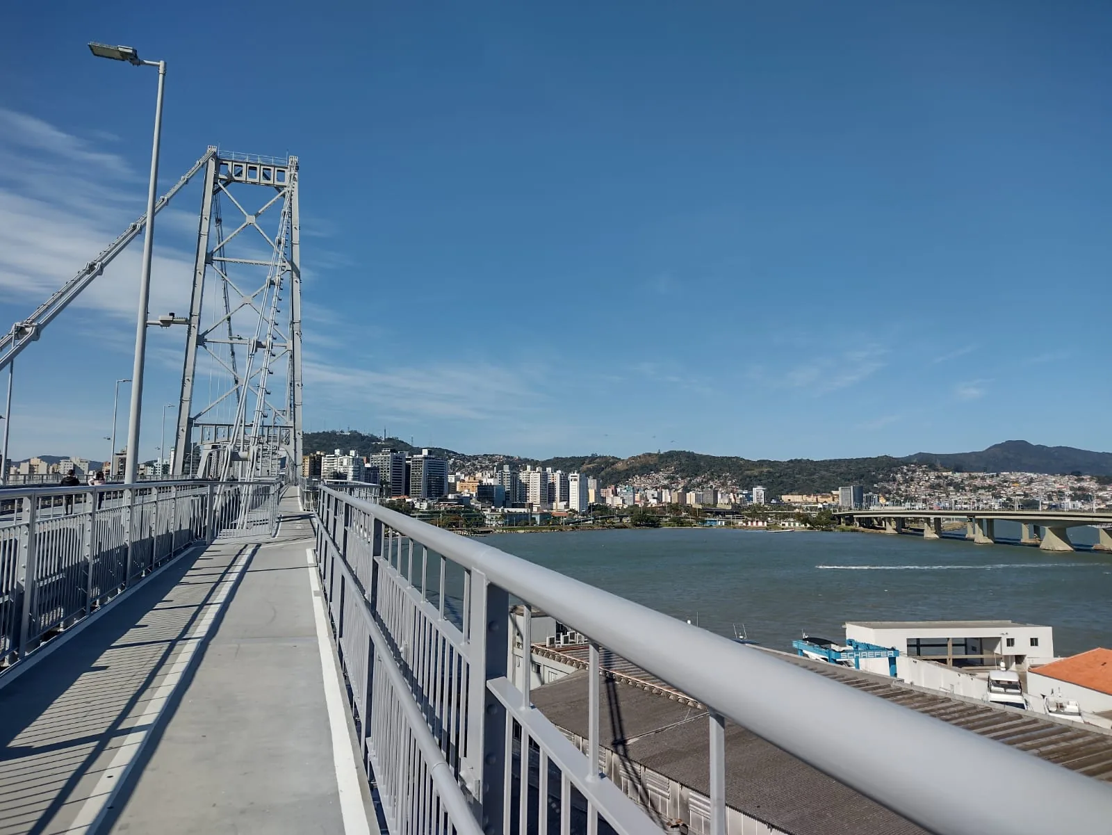 Pista e passarela da Ponte Hercílio Luz vistas por quem atravessa a pé, com a estrutura metálica e o mar ao lado