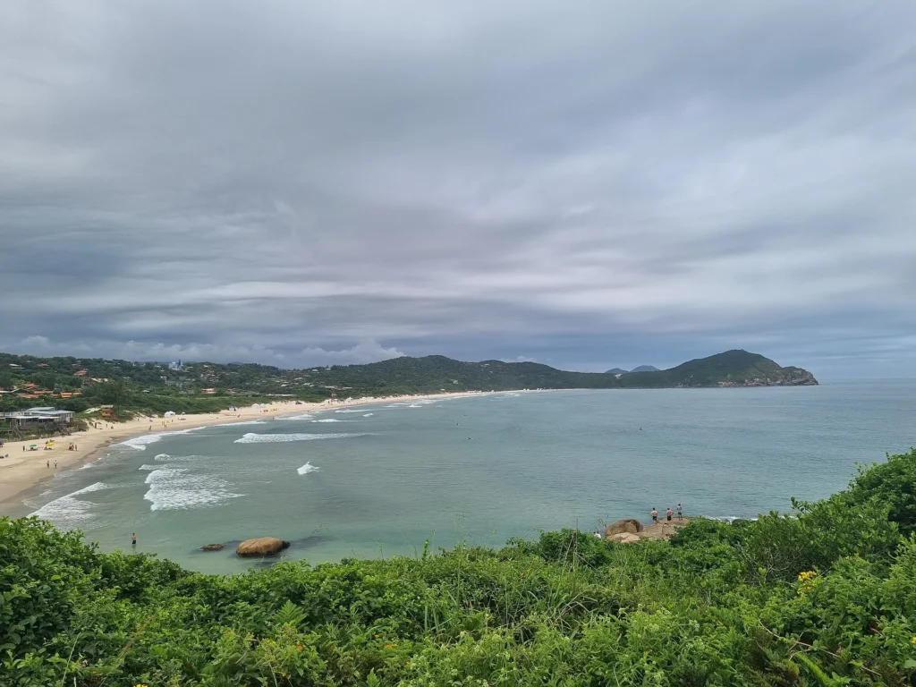 Enseada da Praia do Rosa vista do alto do morro, com faixa de areia em curva, mar azul-esverdeado e morros cobertos de vegetação